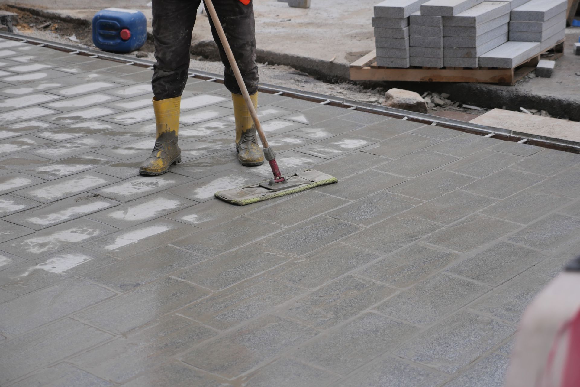 Worker smoothing paving stones on a sidewalk with a trowel and bucket nearby