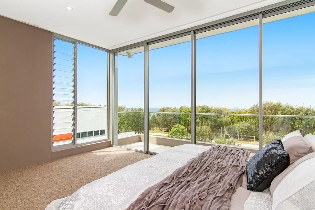 Bedroom with large windows offering an ocean view. A bed is visible with pillows and a plush blanket. — Maryborough Bay Glass & Aluminium in Maryborough, QLD