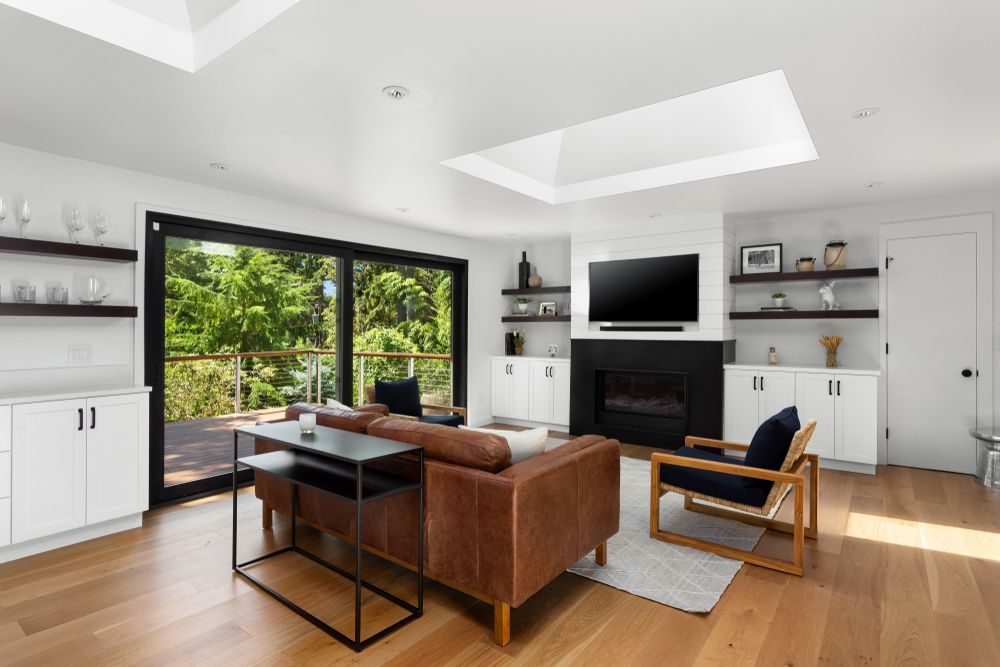 Modern living room with leather sofa, fireplace, large windows, and hardwood floors. — Maryborough Bay Glass & Aluminium in Maryborough, QLD