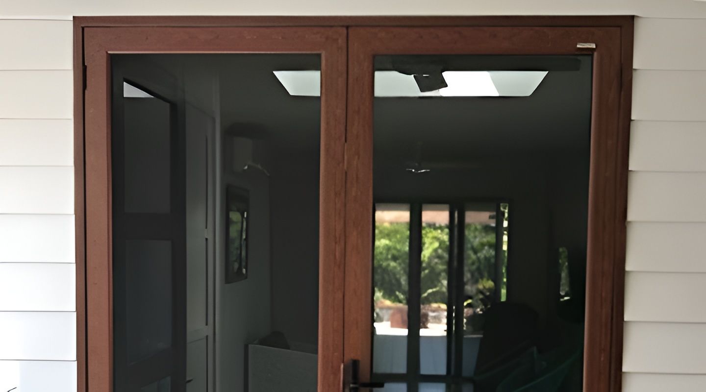 Brown double doors with screen doors set in a white building facade. The doors are open, revealing the interior of a room. — Maryborough Bay Glass & Aluminium in Howard, QLD