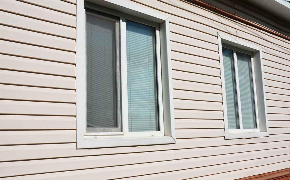 Two windows on a beige vinyl-sided building. One window has a screen and blinds. The other window has blinds. — Maryborough Bay Glass & Aluminium in Maryborough, QLD