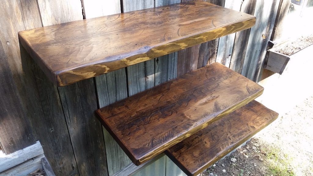A wooden shelf with three shelves is sitting in front of a wooden wall.