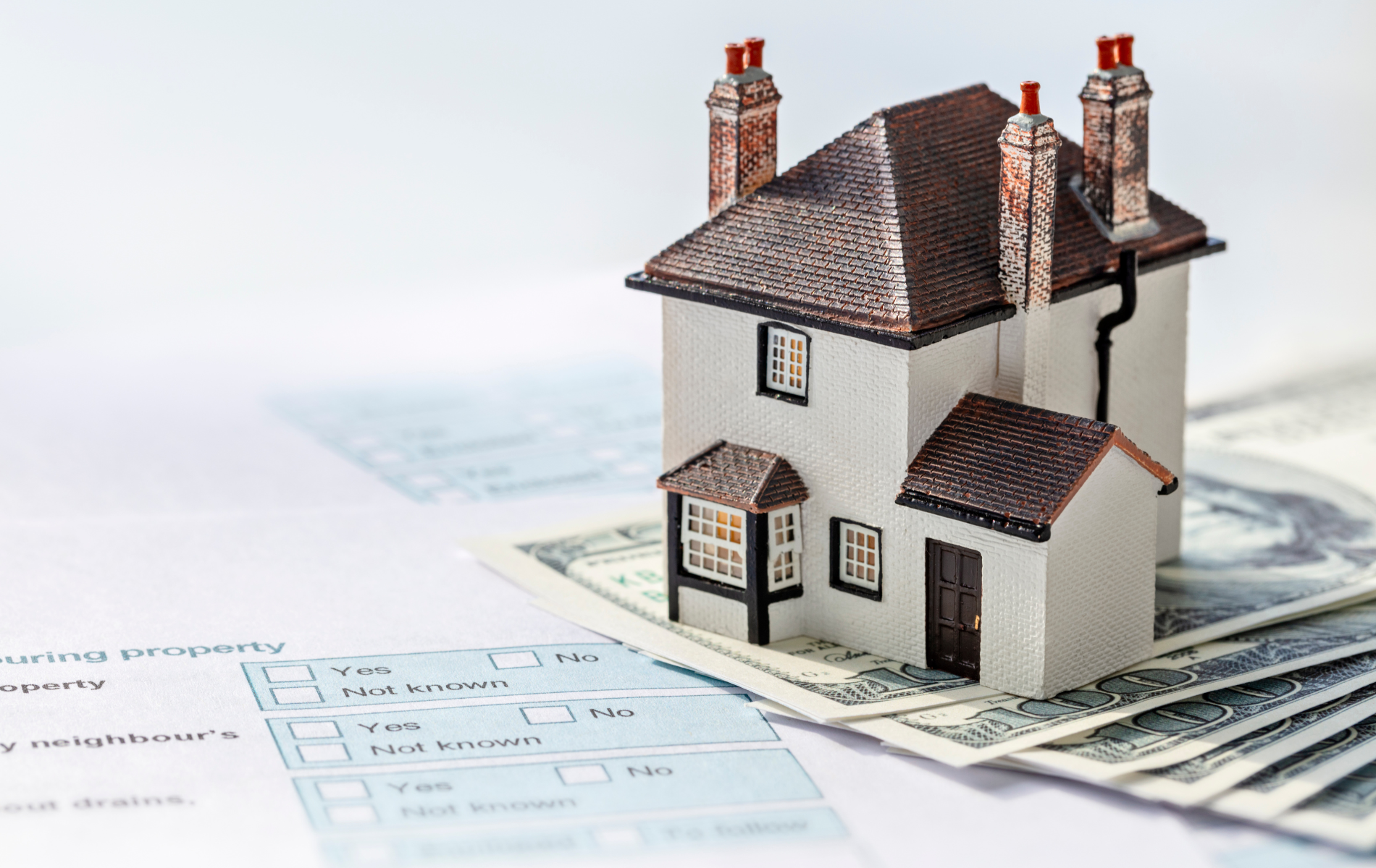 A model house is sitting on top of a pile of money.