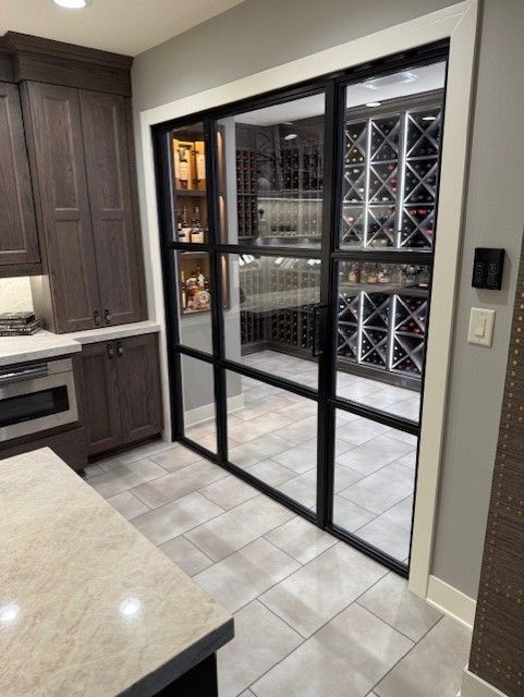 Kitchen with a black-framed glass door opening to a wine storage room with racks and tile flooring.