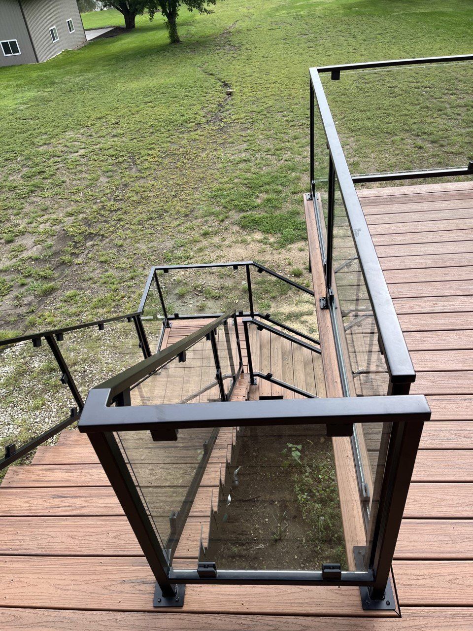 Wooden outdoor stairs with black railings descending from a deck to a grassy yard.