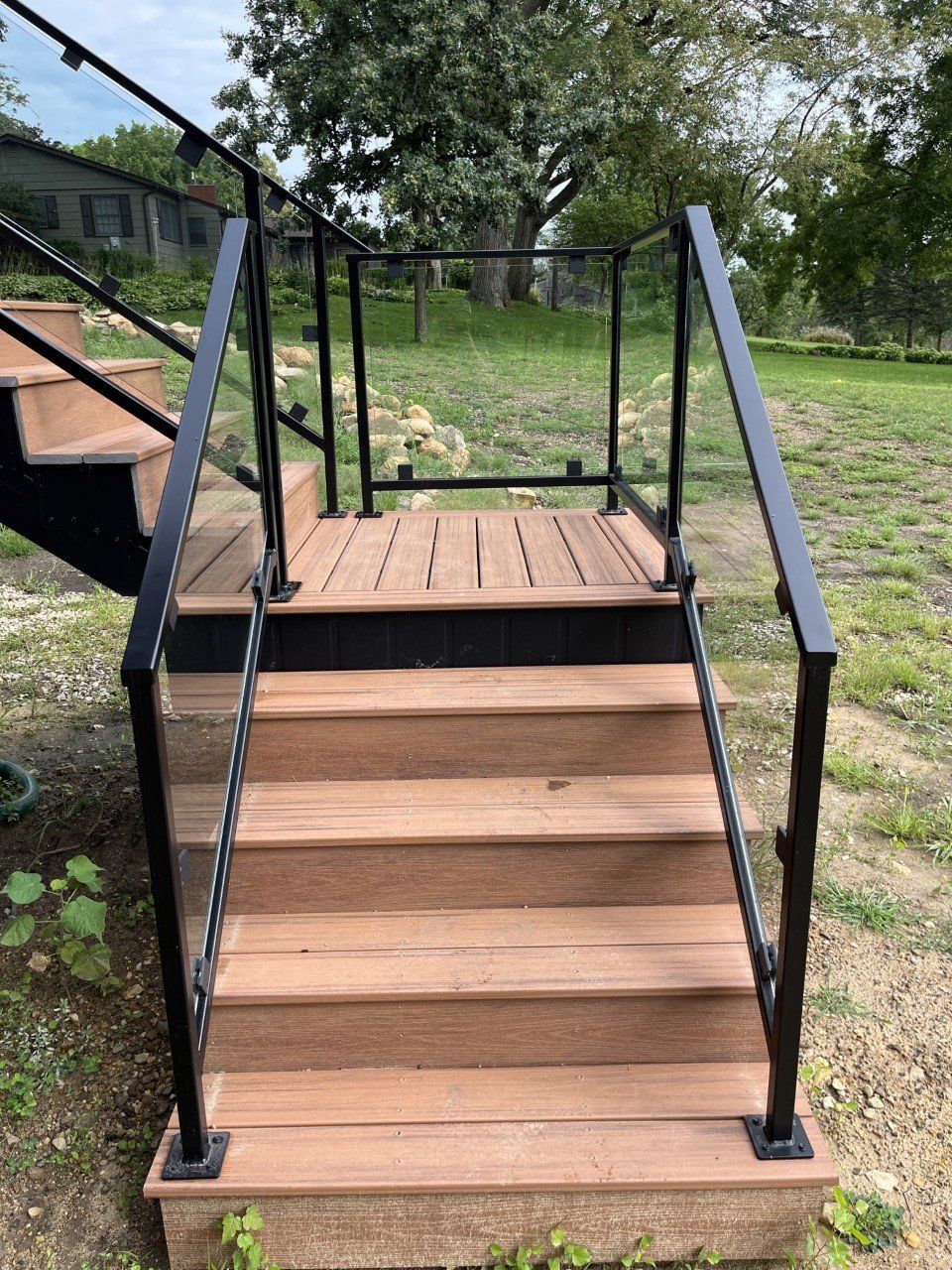 Wooden wheelchair ramp with black railings leading to a raised outdoor platform in a grassy yard