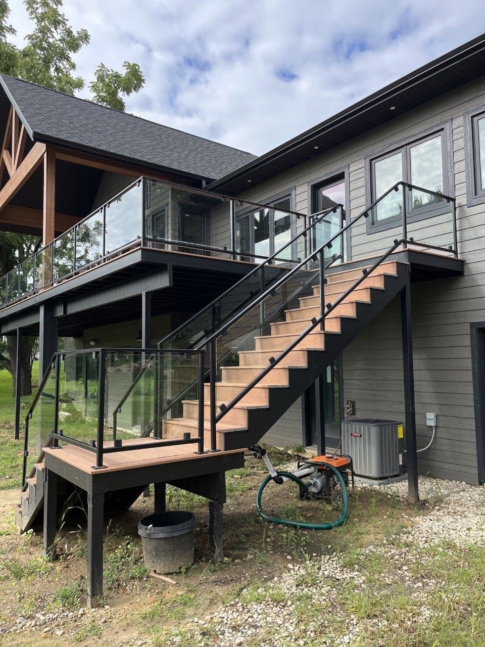 Exterior staircase with black railings leading to a raised deck on a gray house under a cloudy sky