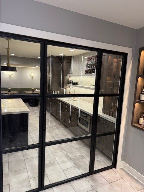 Modern kitchen viewed through black-framed glass doors, with gray walls and light countertops.