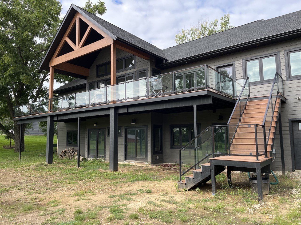 Modern house on stilts with a glass balcony and exterior stairs in a grassy yard