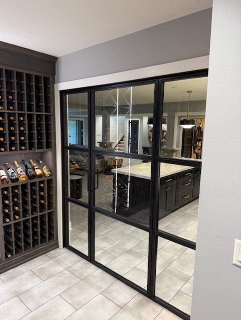 Glass sliding doors reveal a wine room with black racks and tiled floors.