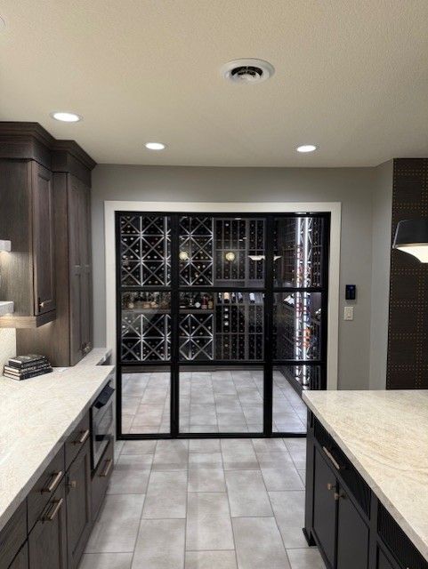 Modern kitchen with dark cabinets, white countertops, and a glass wine display wall at the end.