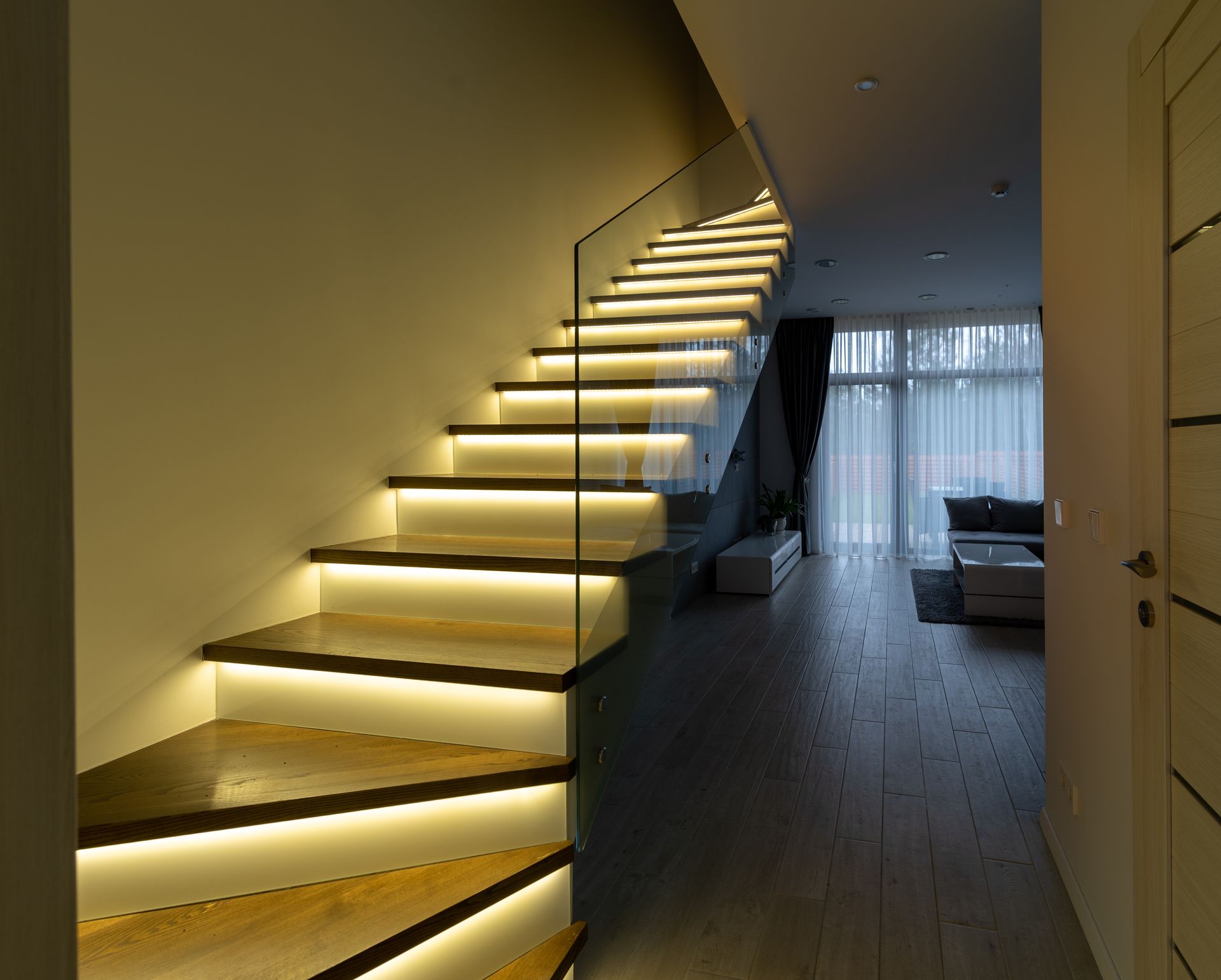 Modern staircase with LED-lit wood treads and a glass railing, a popular railing services upgrade