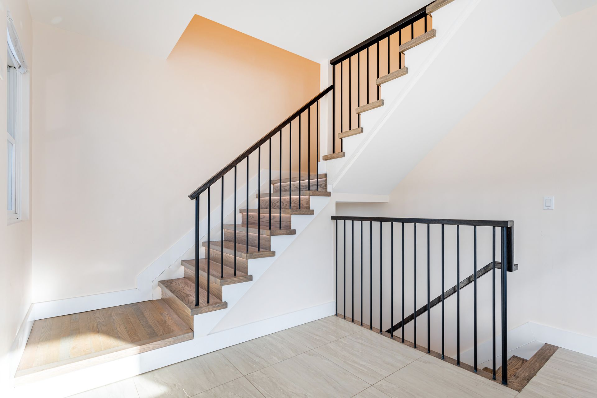 Interior railing contractors install black metal balusters along wood stairs and a landing