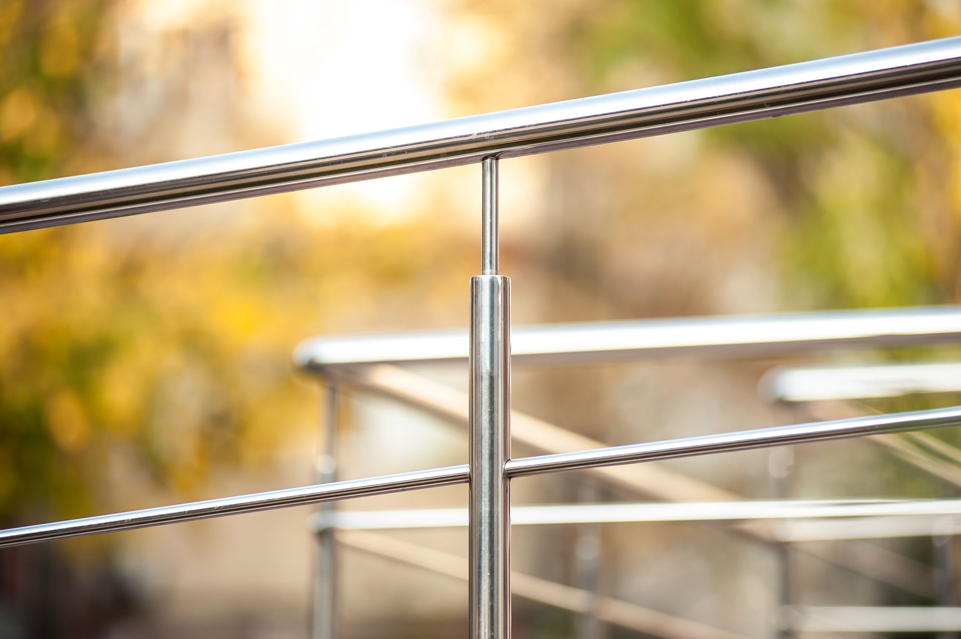 Polished stainless steel handrail with blurred foliage background.