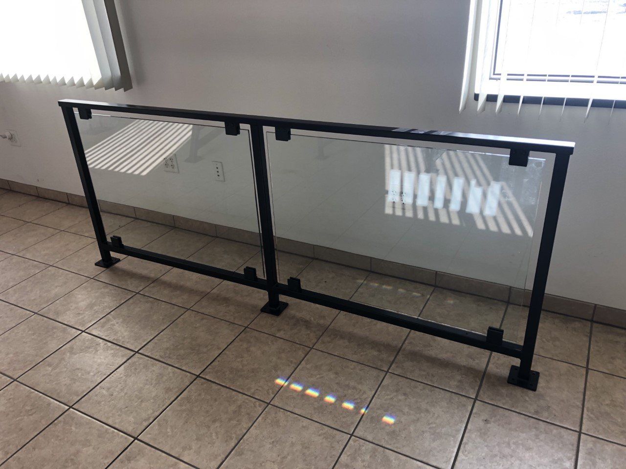 Black metal-and-glass safety barrier on tiled floor beside a wall with windows.