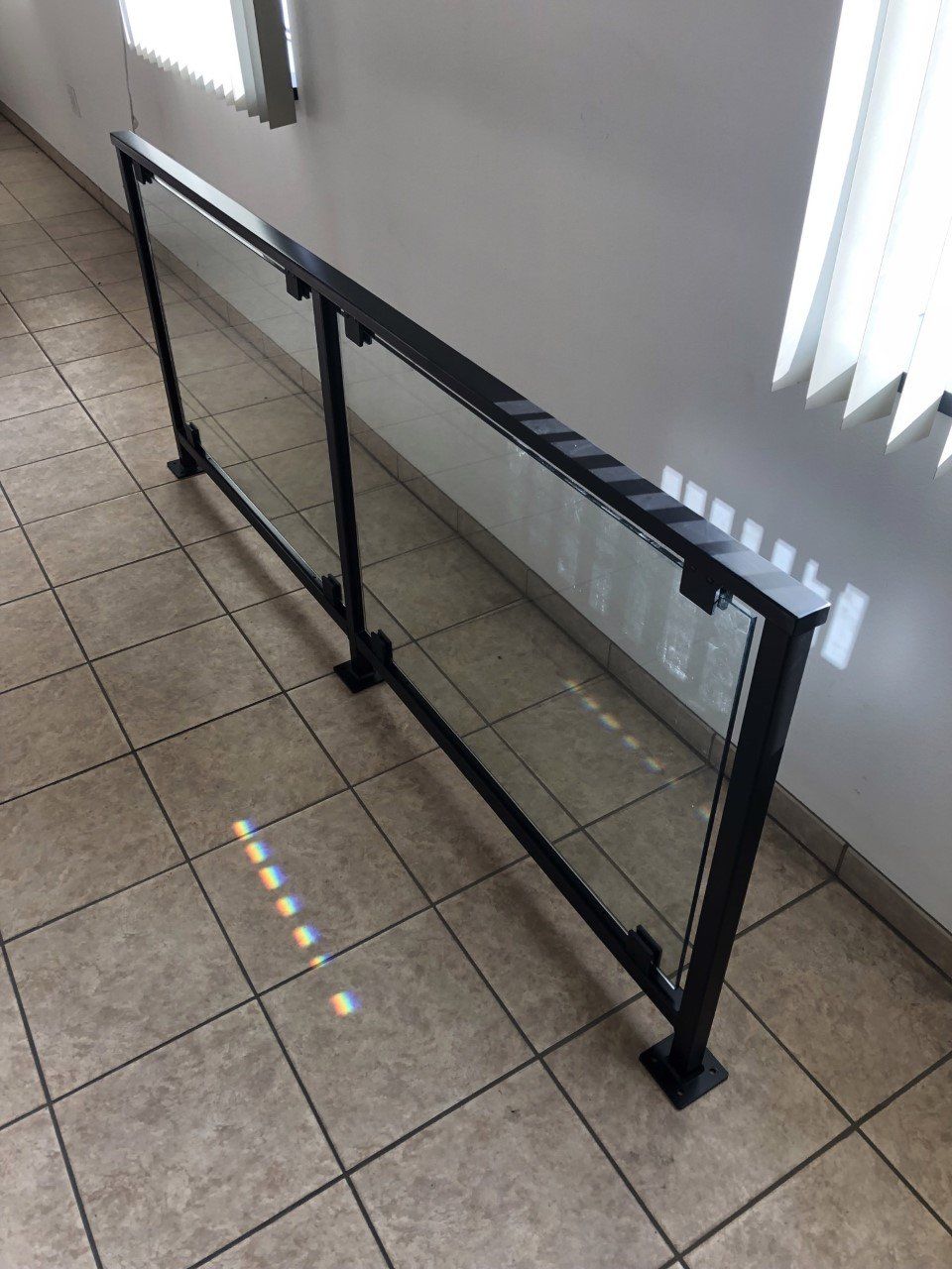 Black metal safety barrier along a tiled indoor hallway beside a wall and window blinds.