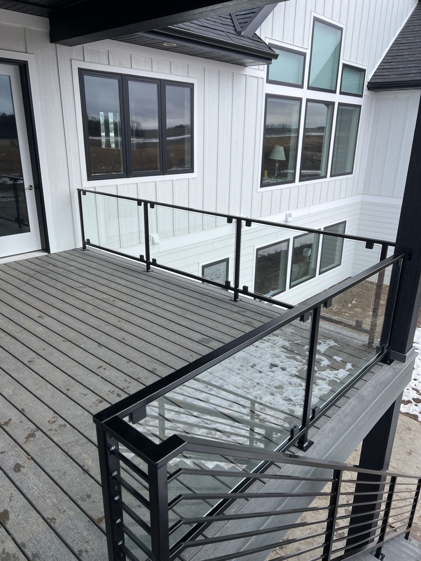 Snowy rooftop deck with black metal railing and stairs beside a white building