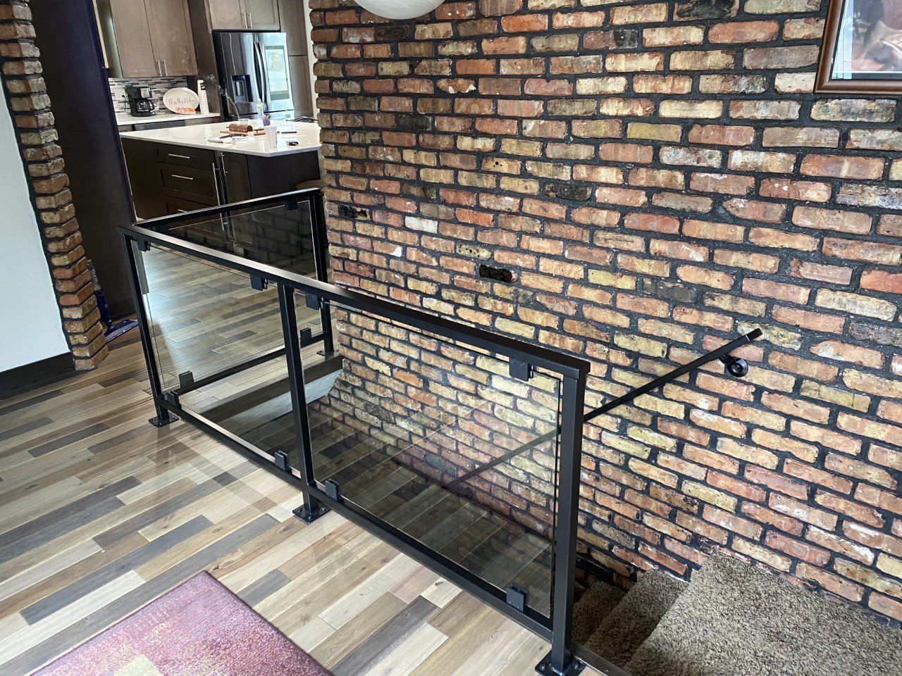 Black metal railing along a brick wall beside a staircase in an indoor hallway