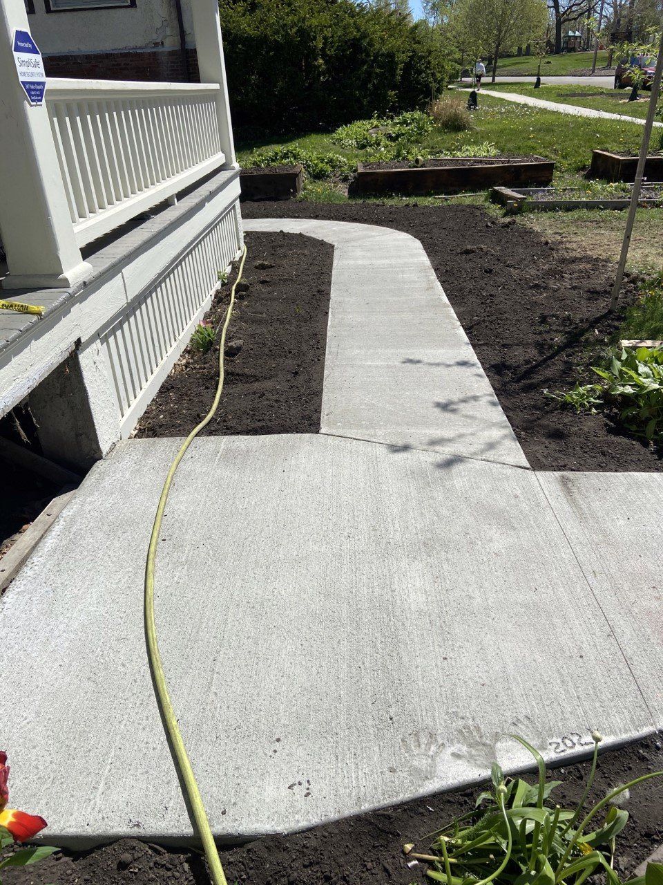 Concrete walkway beside a porch, with fresh dark mulch beds and a yellow hose running along the path.
