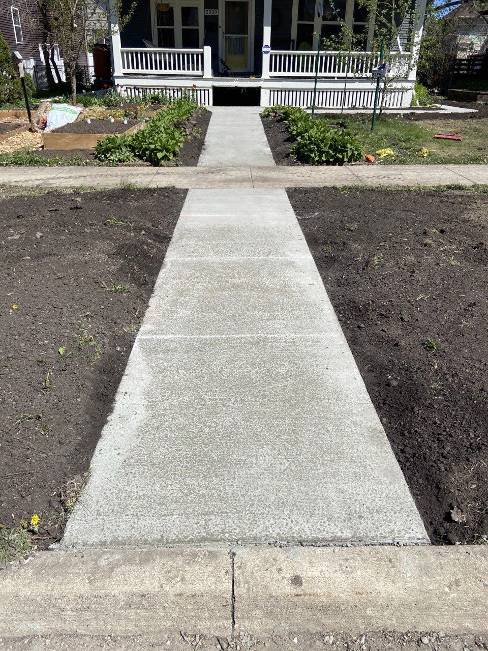 Concrete walkway leading to a front porch with white railing, bordered by bare garden beds