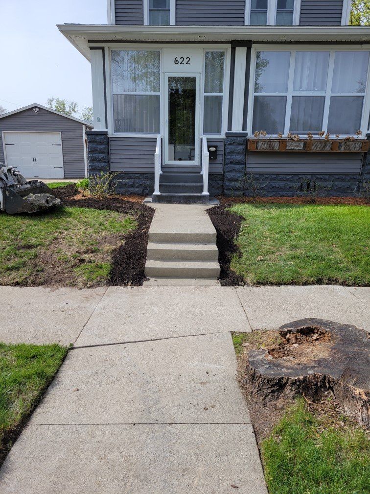Front walkway to a small house with concrete steps, a front door, and a tree stump in the yard.