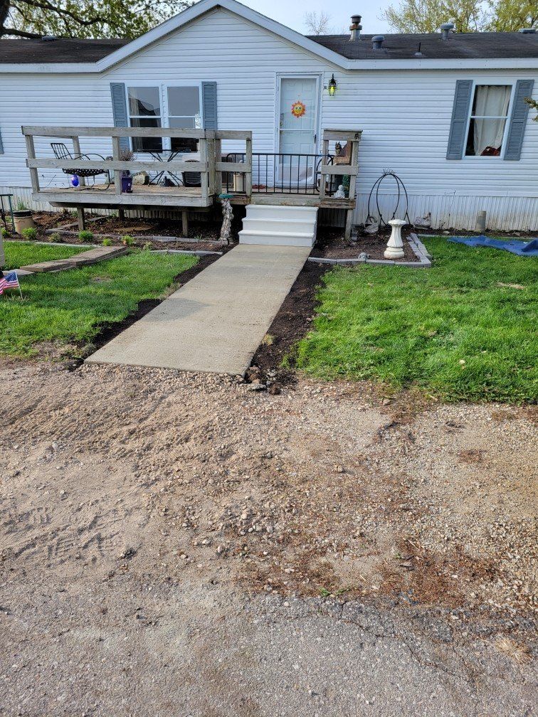 Small house with front ramp, porch railing, and lawn, viewed from the driveway.