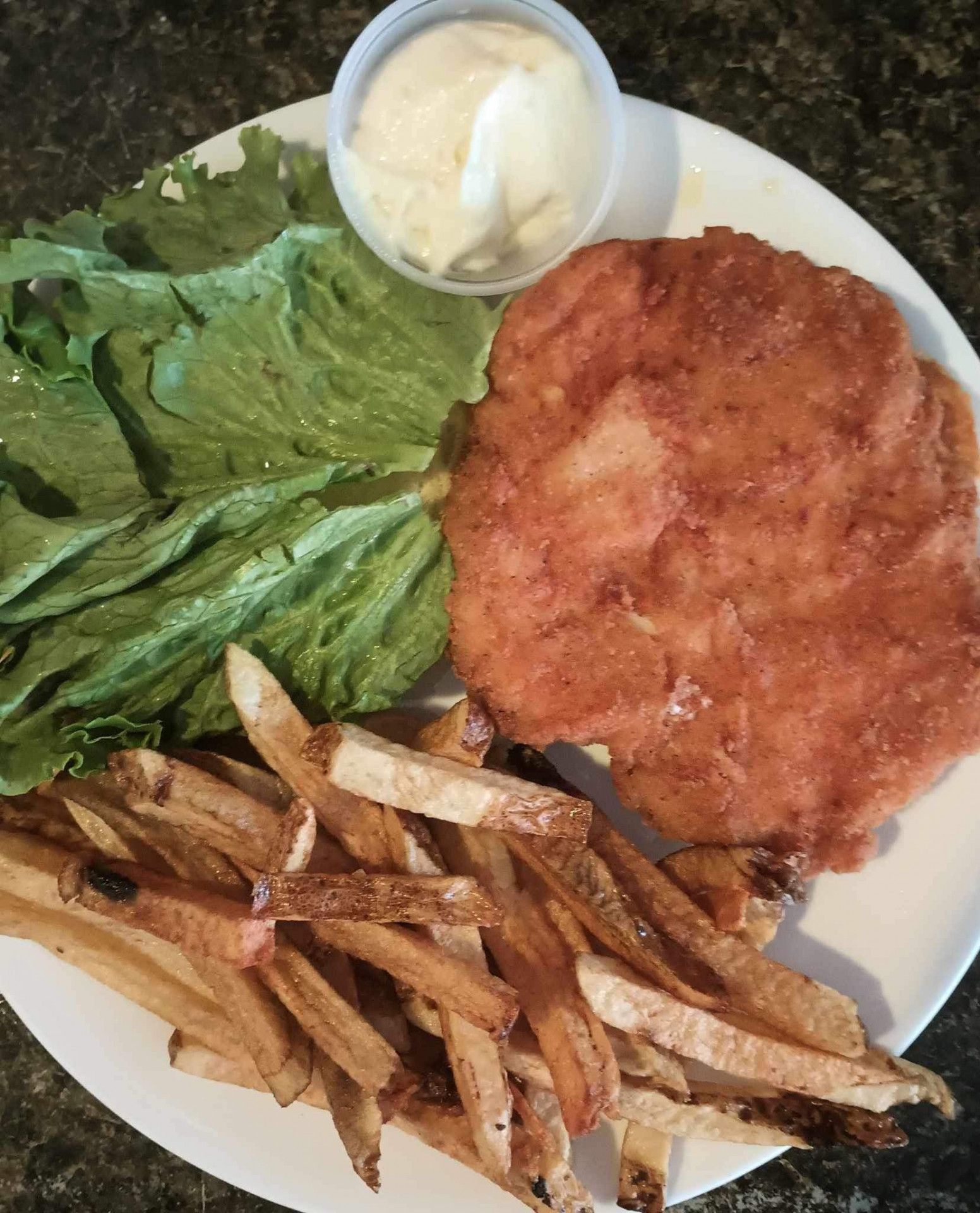A white plate topped with french fries , lettuce and a fried chicken sandwich.