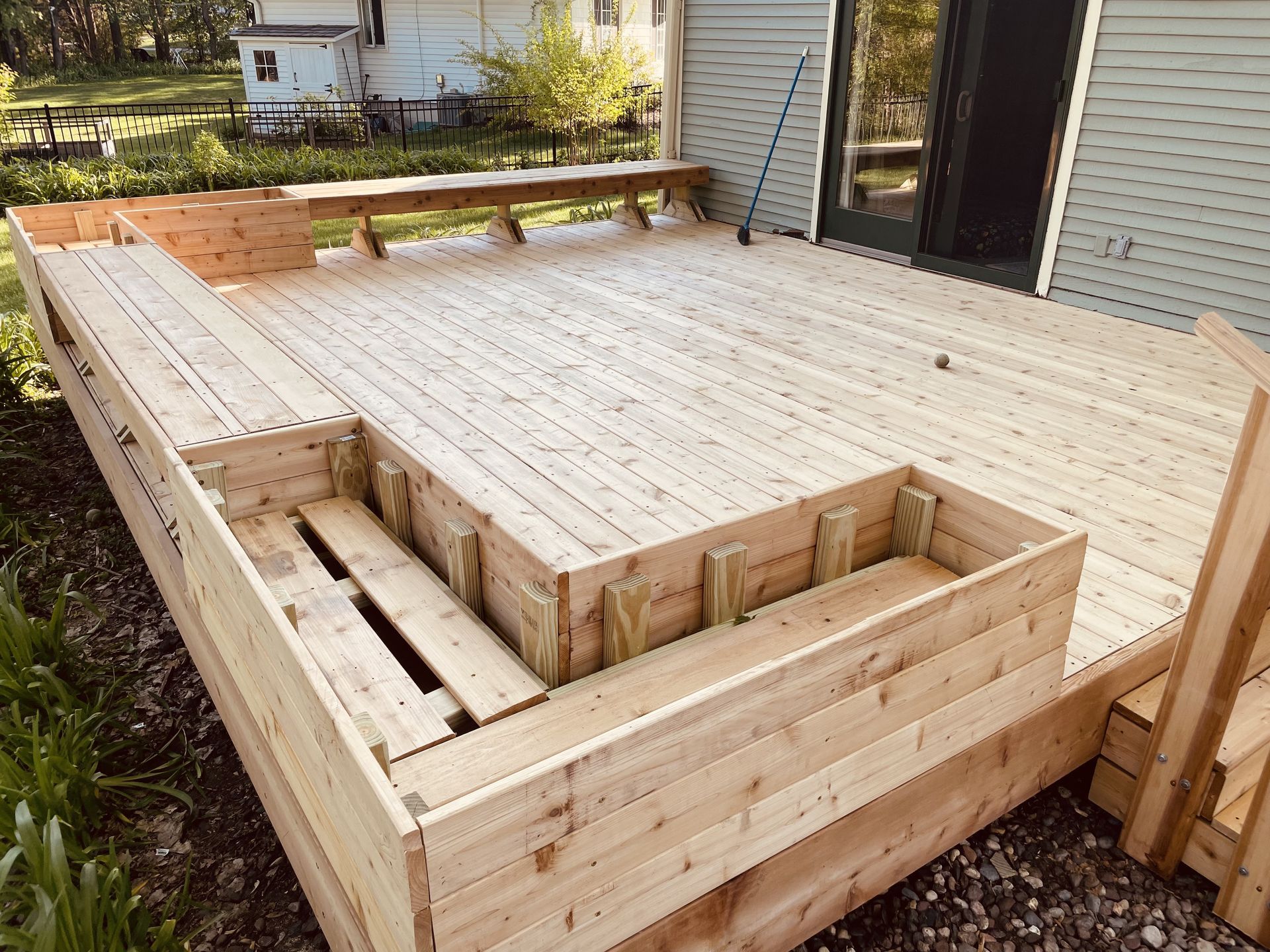New wooden deck with built-in steps, bench, and various levels; beside a house.