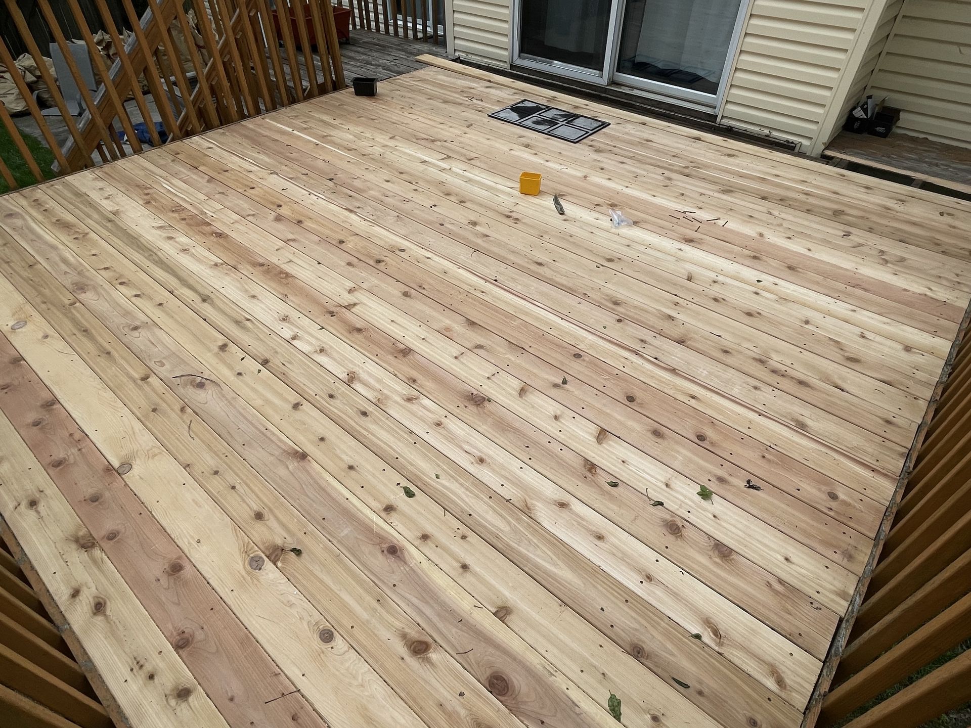 Newly built wooden deck with light-colored planks, adjacent to a beige house with a sliding glass door.