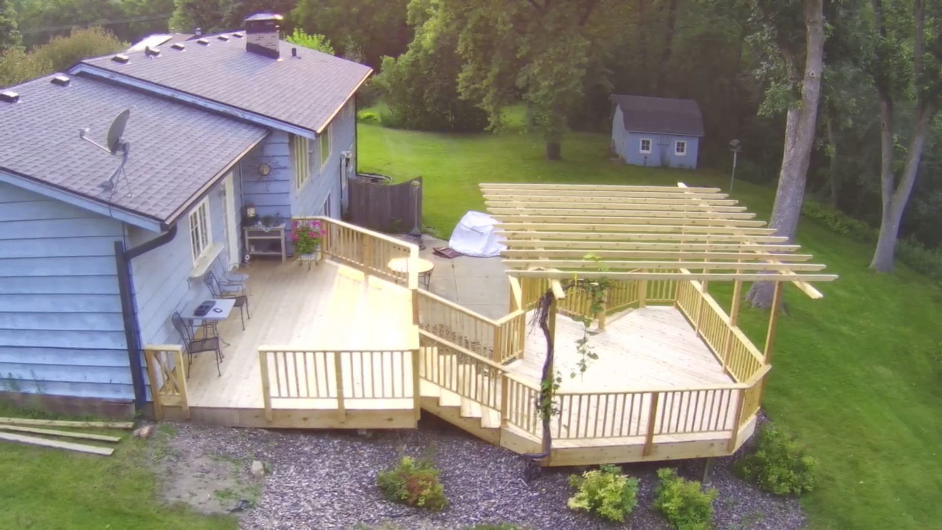 Elevated view of a blue house with a multi-level wooden deck, arbor, and lush green lawn.