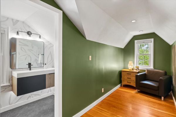 A bedroom with green walls, wooden floor, and a small vanity area.