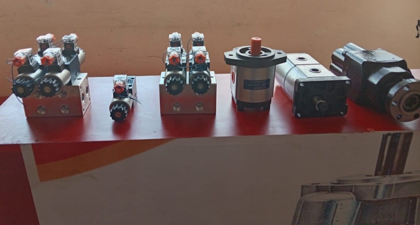 Pequeños componentes mecánicos y accesorios metálicos dispuestos en fila sobre un estante rojo cerca de una pared.