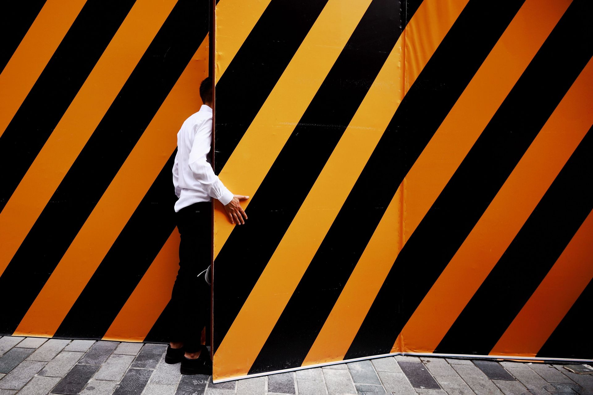 Person in white shirt and black pants walking past a black-and-orange striped wall