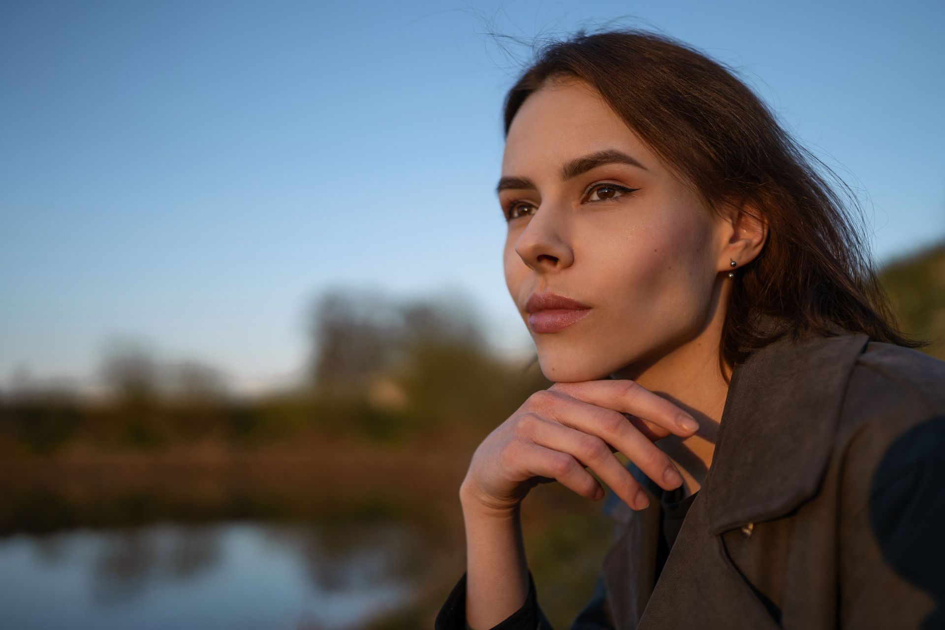 Woman outdoors at sunset, resting her chin on her hand and gazing into the distance.