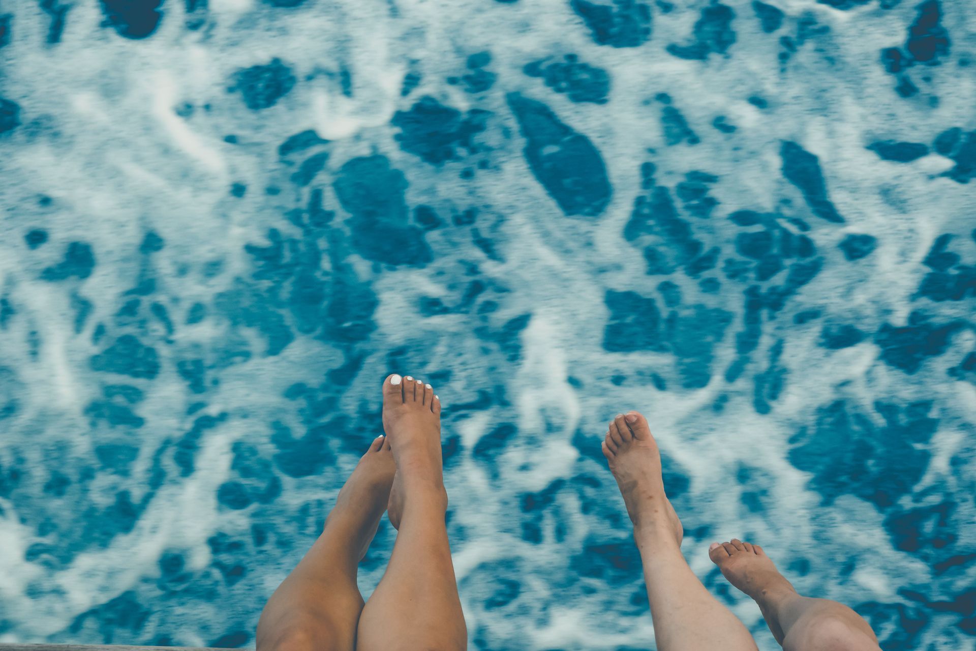 Two pairs of feet over turquoise ocean waves from a boat or dock