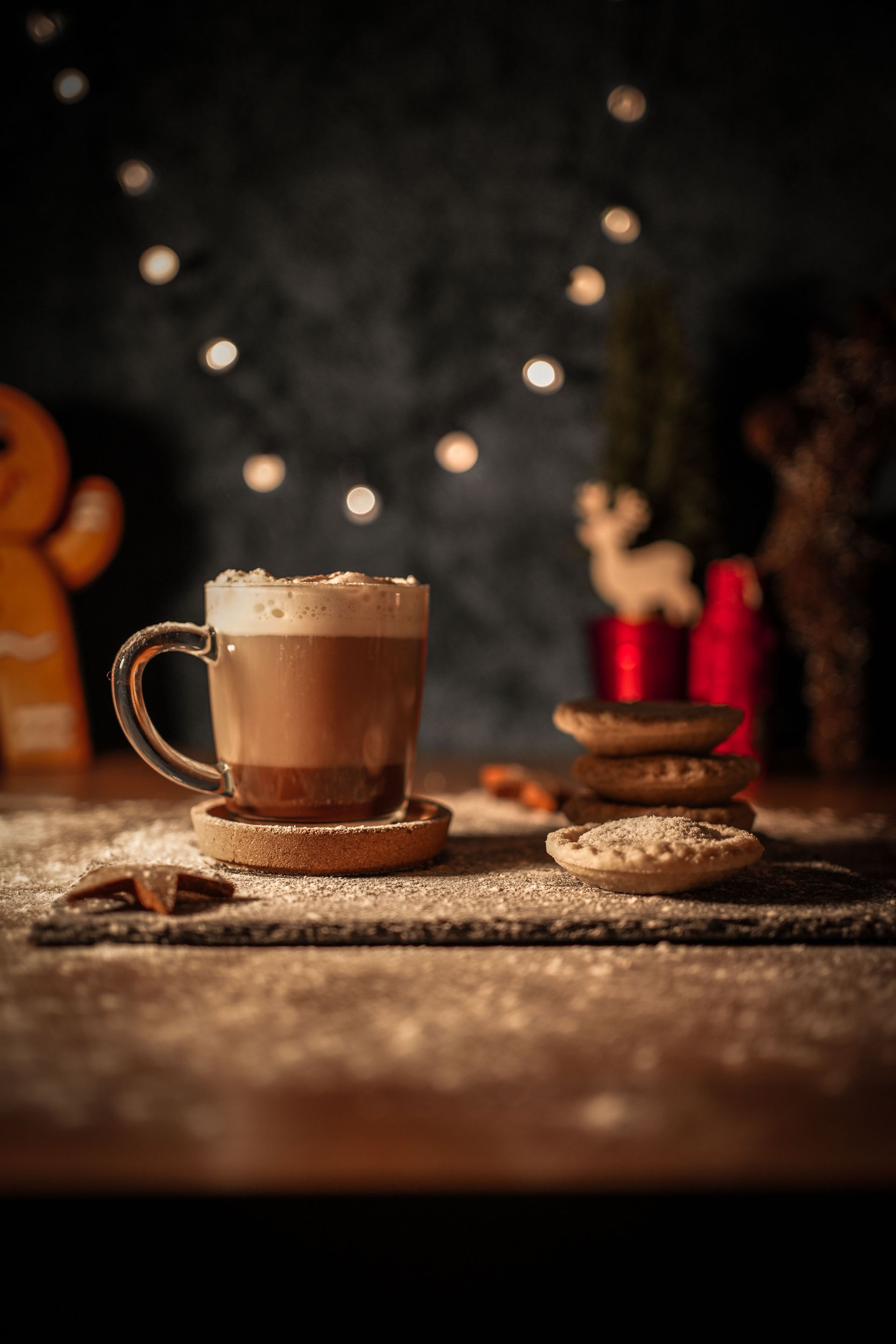 Cozy coffee scene with a steaming mug, cookies, and festive bokeh lights on a rustic table