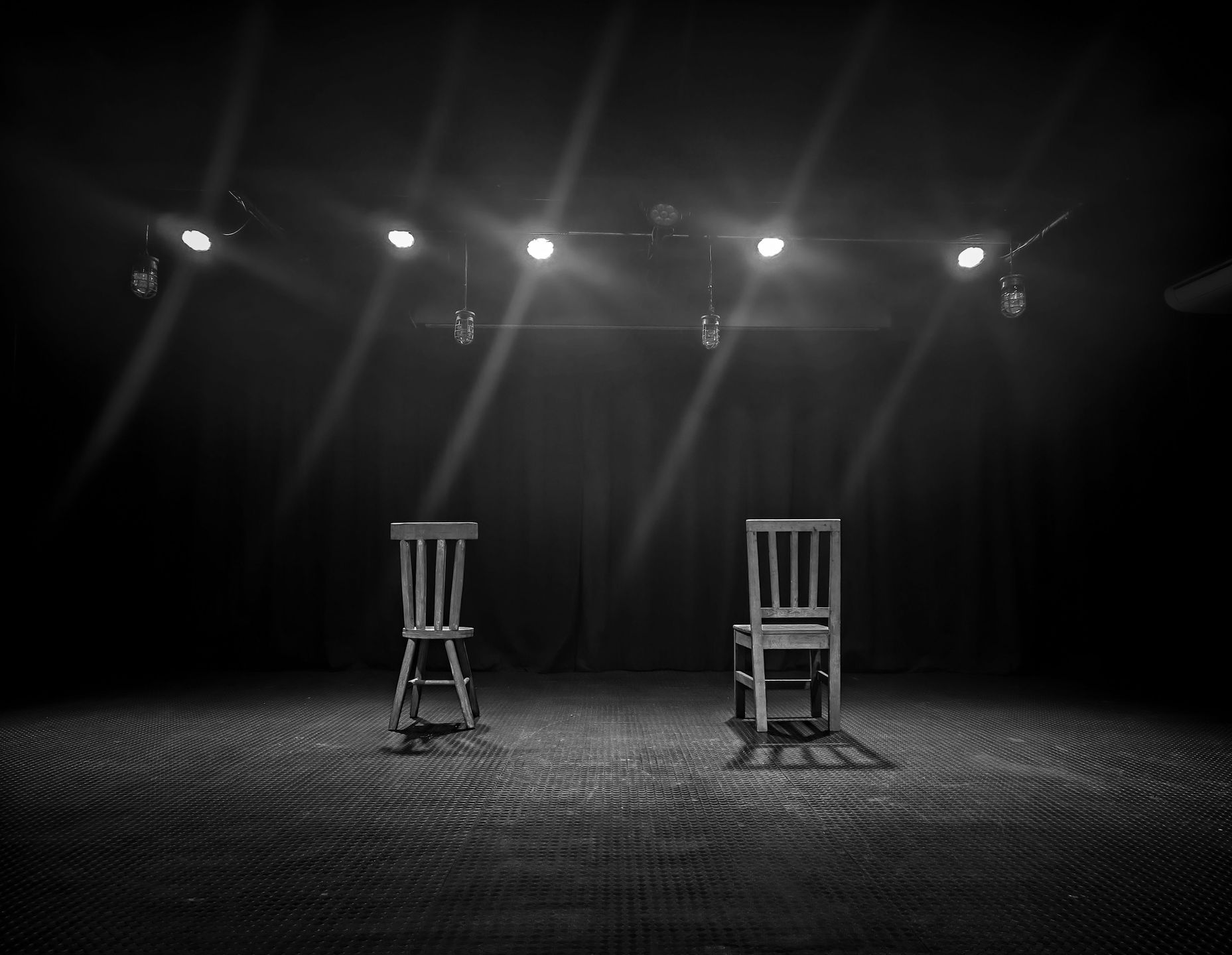 Two empty wooden chairs under spotlights on a dark stage