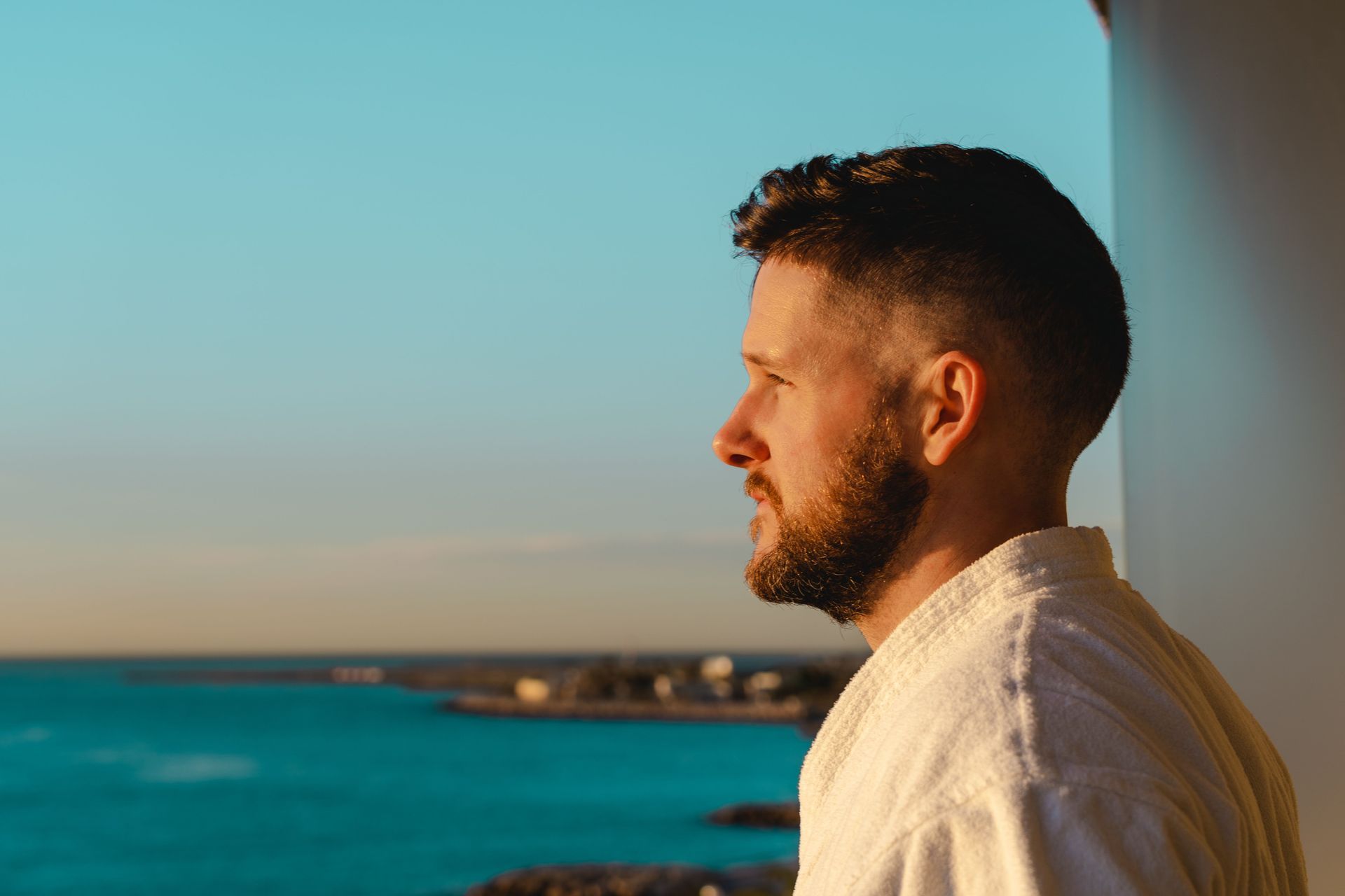 Man in white shirt looking out over a blue ocean at sunset