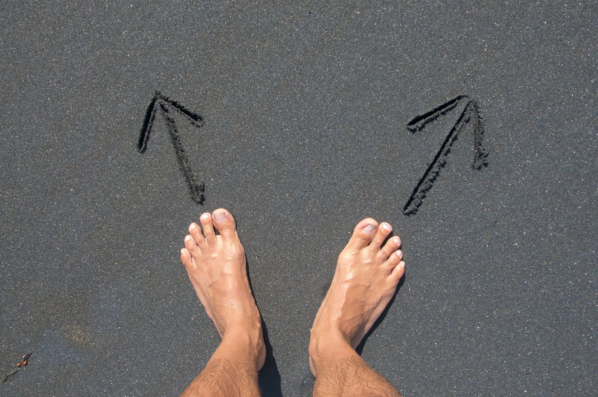 Bare feet on dark pavement with two hand-drawn arrows pointing outward toward the left and right feet