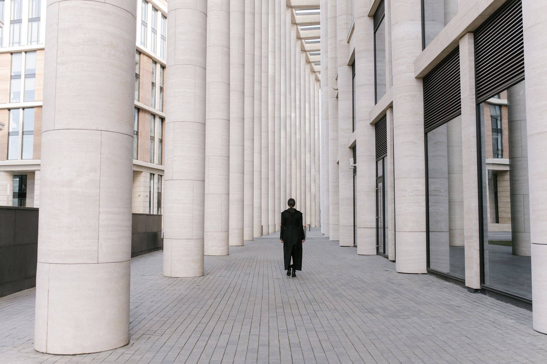 Person walking through a modern colonnade of white columns and glass walls
