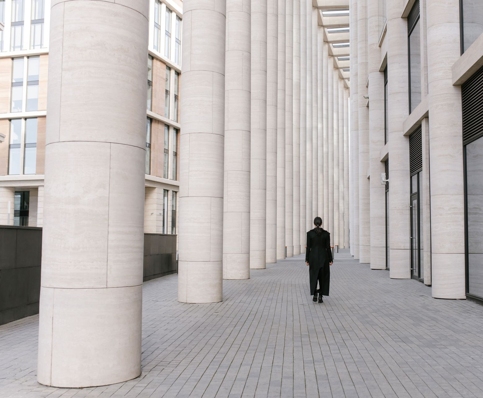 Lone person in dark clothing walking through a colonnade of tall white columns