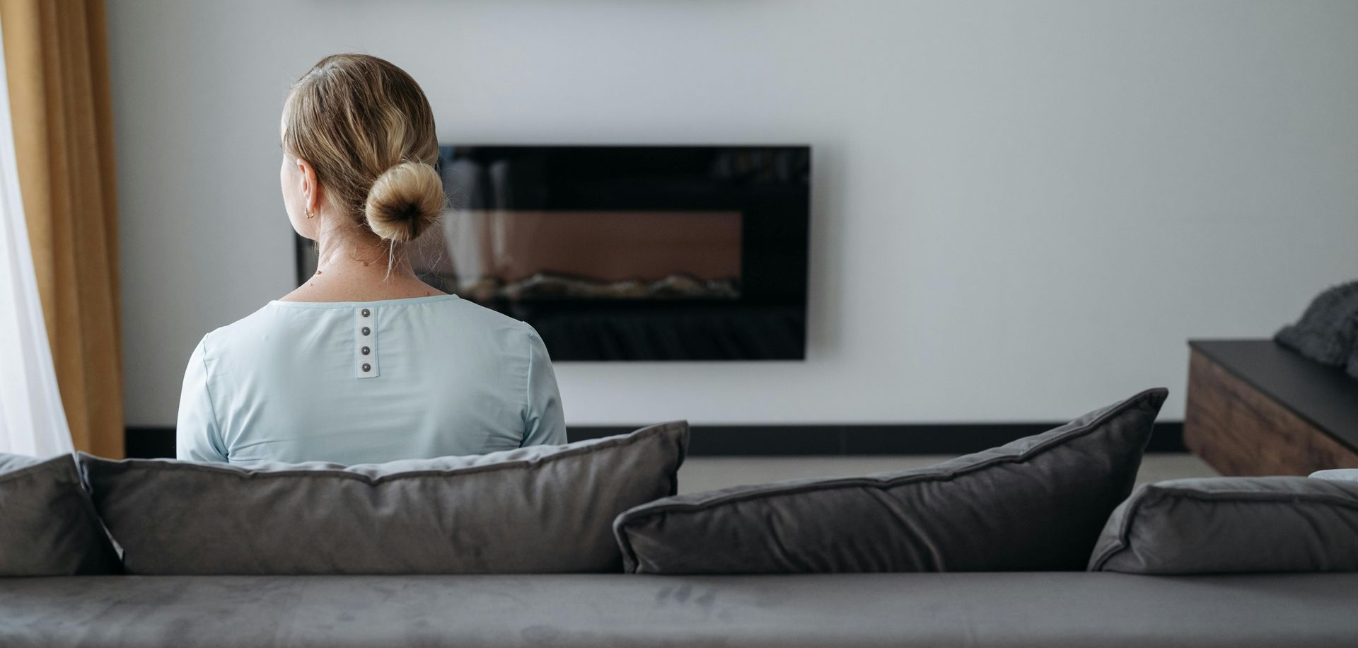 Woman sitting on a sofa, facing away, in quiet reflection. A symbolic image of grief, loss, and the journey of healing.