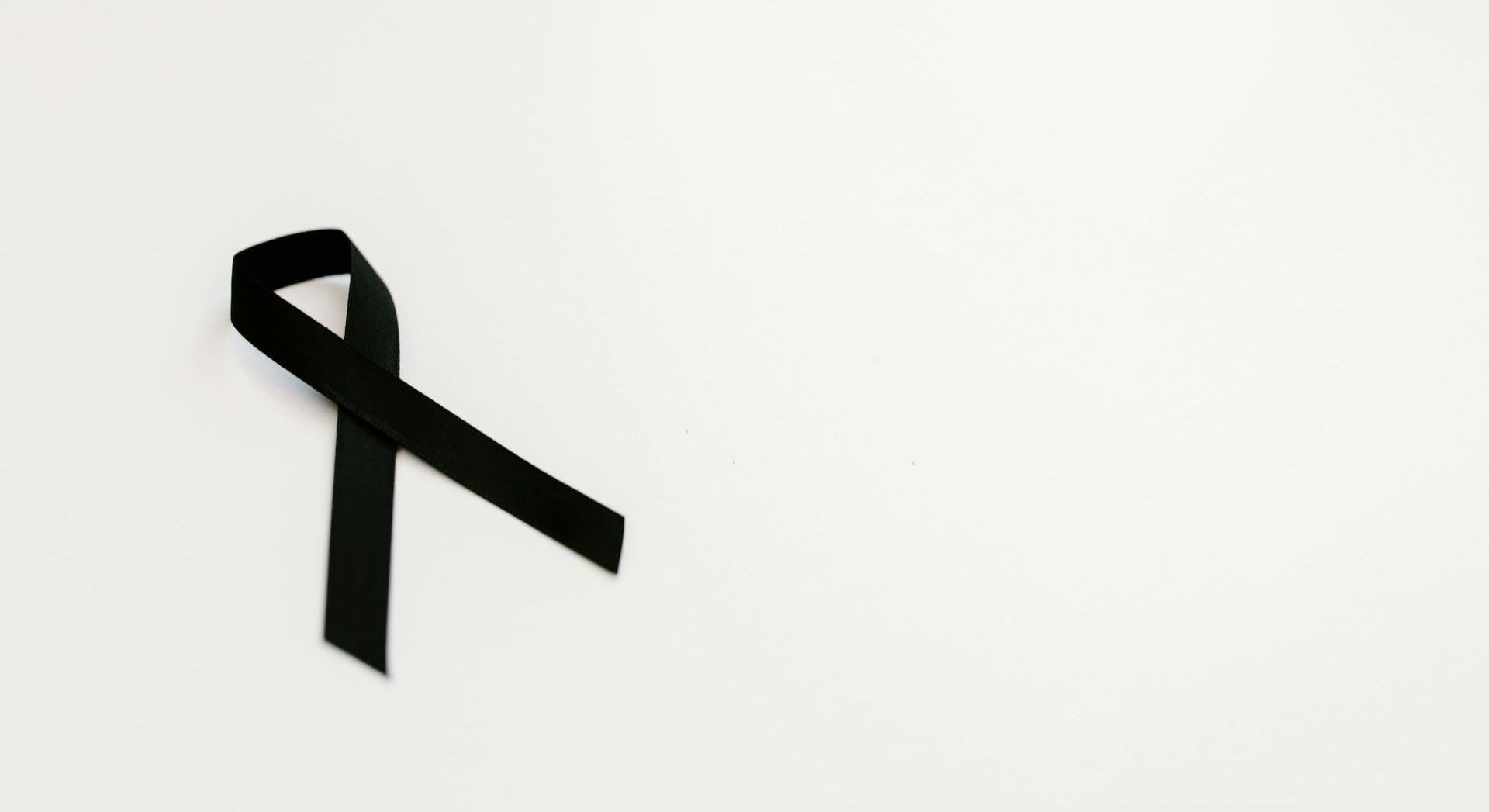 A black ribbon on a plain white background, symbolising mourning, remembrance, and the process of grief.