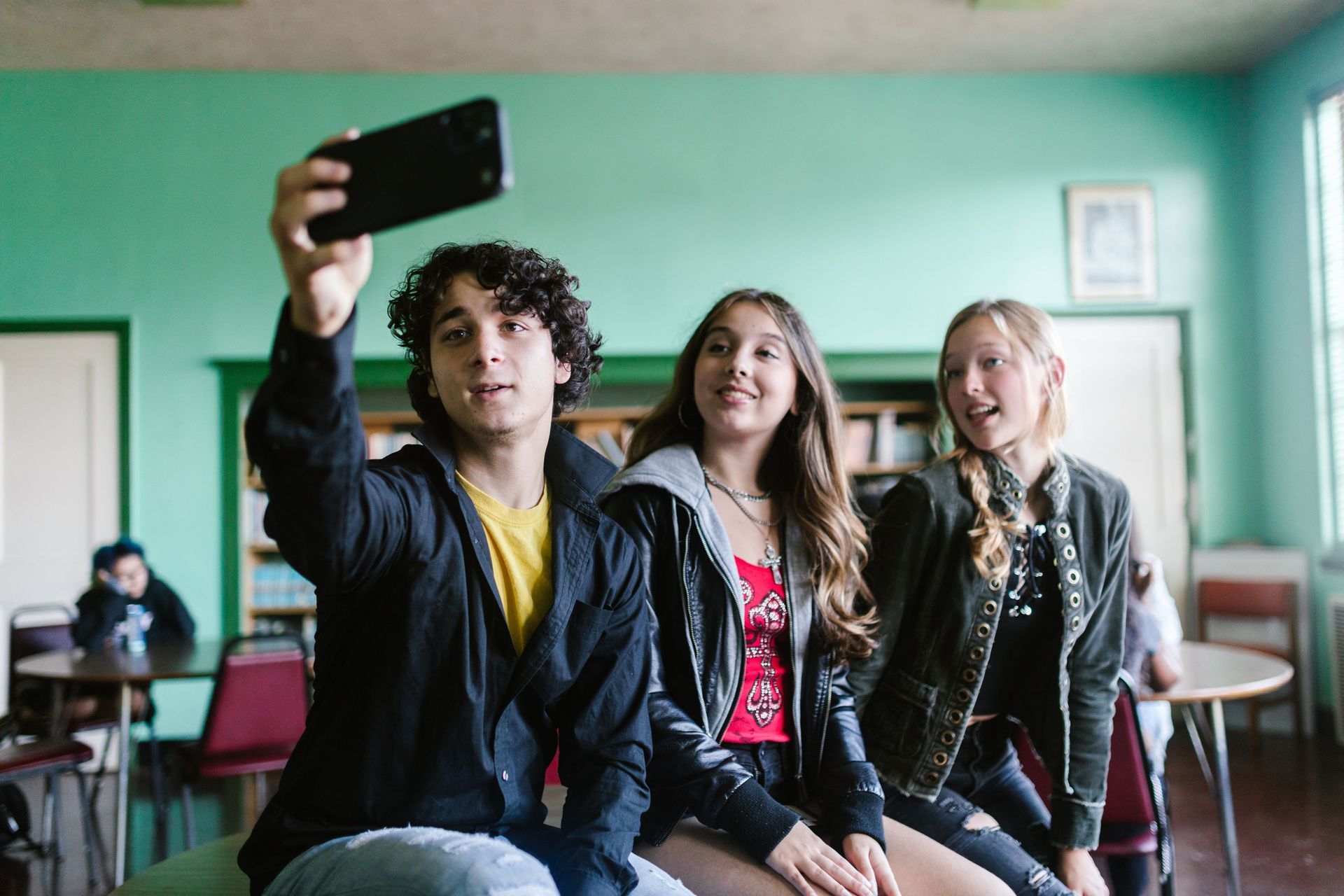 Three students in a classroom taking a selfie, smiling with a phone held up