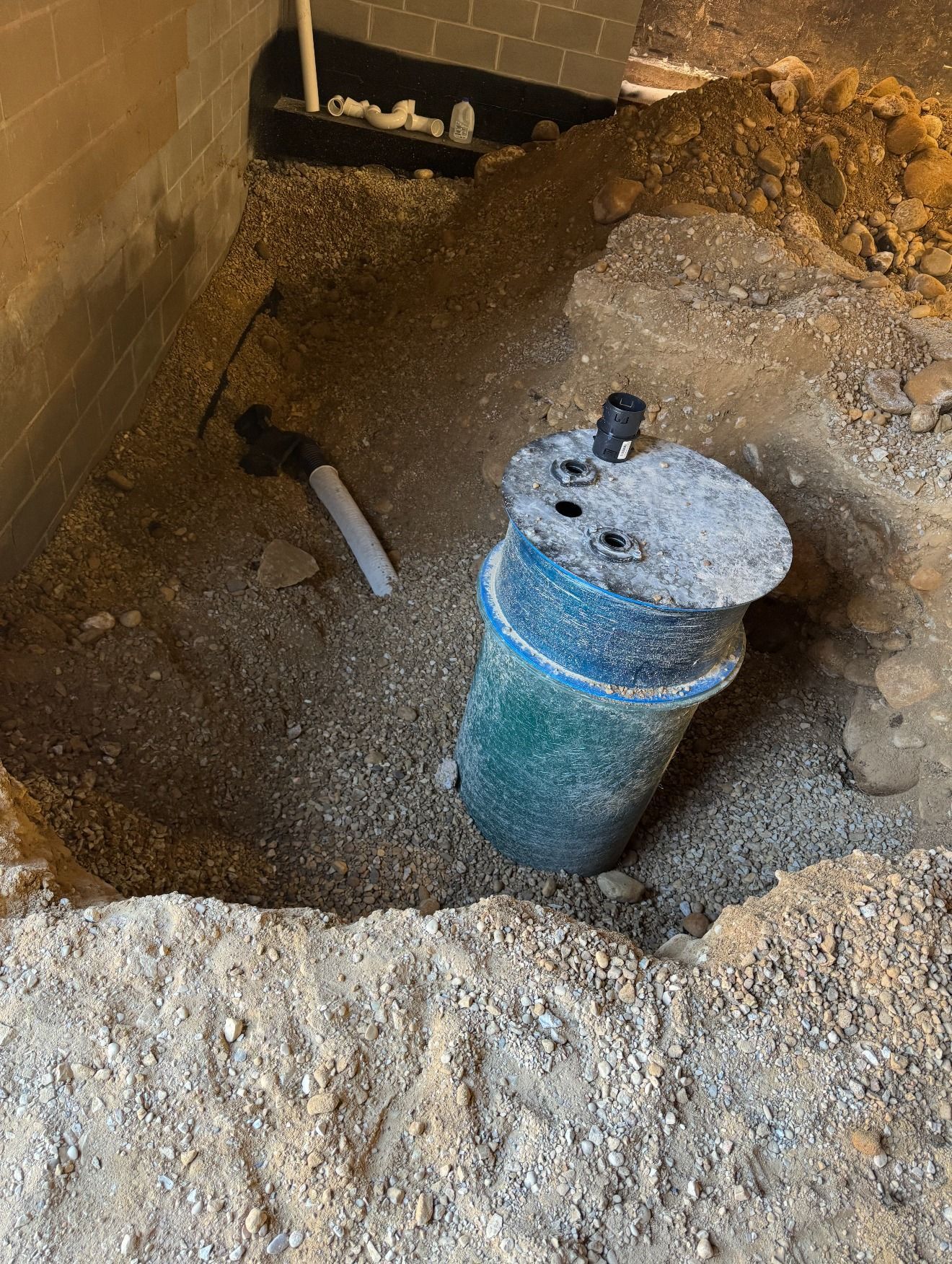 Basement excavation with a blue capped pipe in a dirt pit near a brick wall