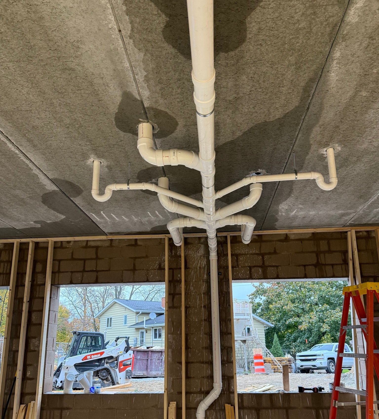 Ceiling view of exposed white plumbing pipes in an unfinished room under construction