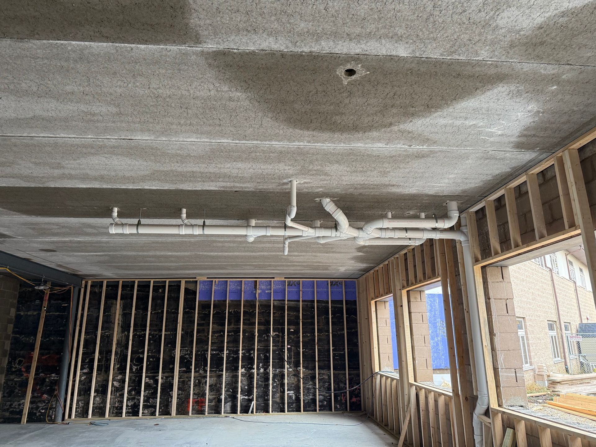 Partially renovated room with exposed framing, concrete ceiling, and windows on the right and back walls