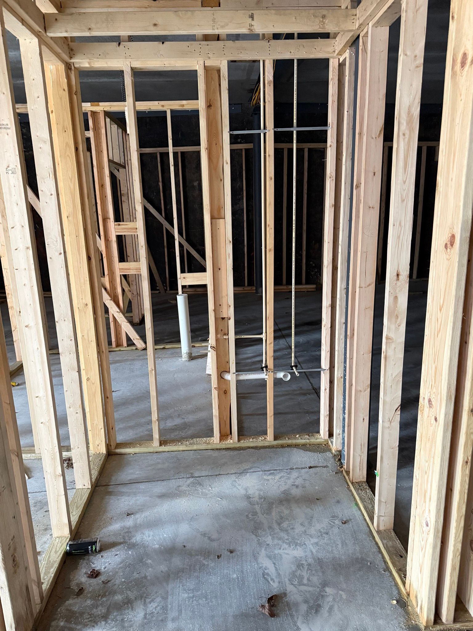Interior of a framed house under construction, with exposed wooden studs and a concrete floor.