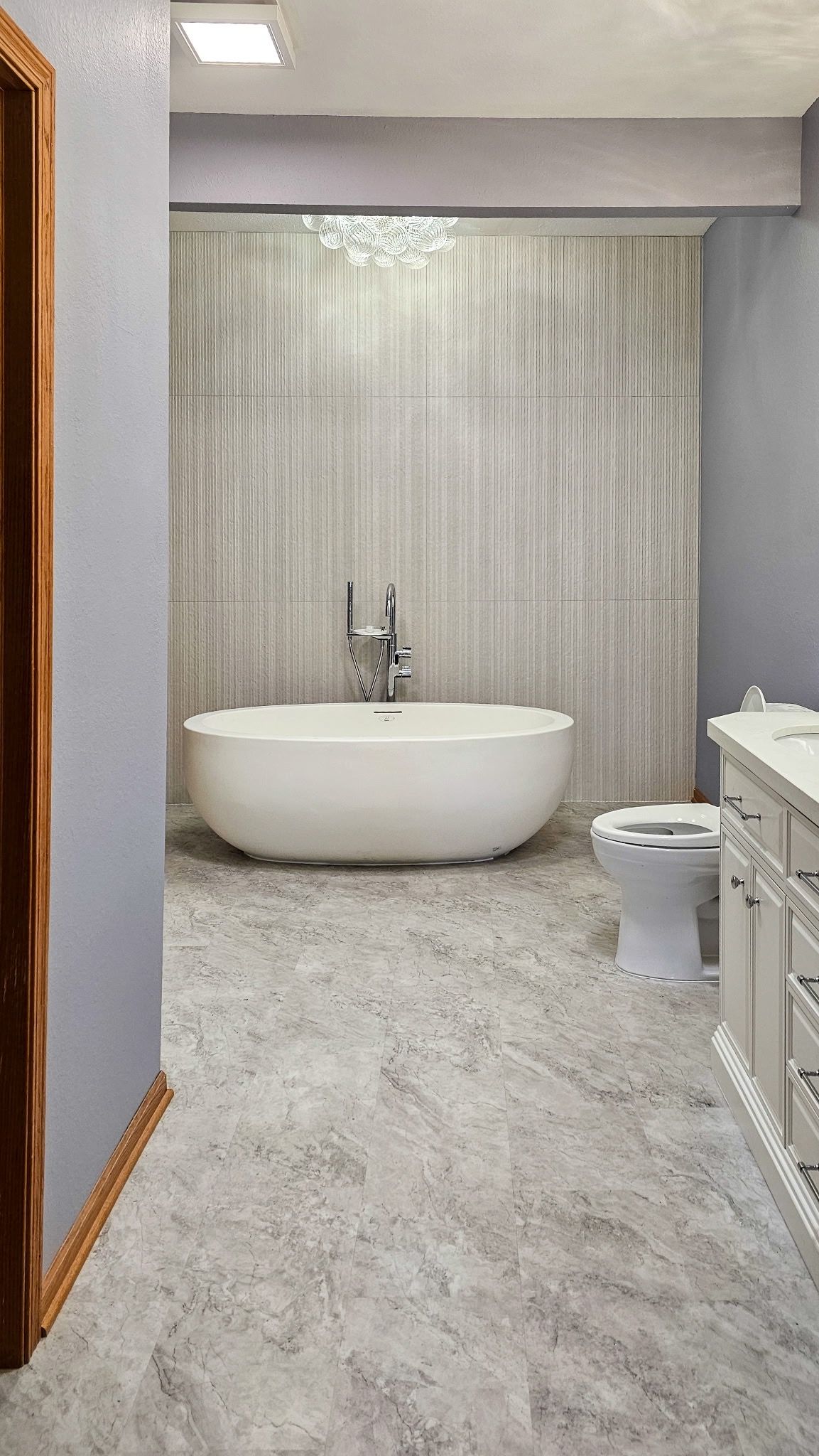 Modern bathroom with a freestanding tub, toilet, and vanity, in gray and white tones.