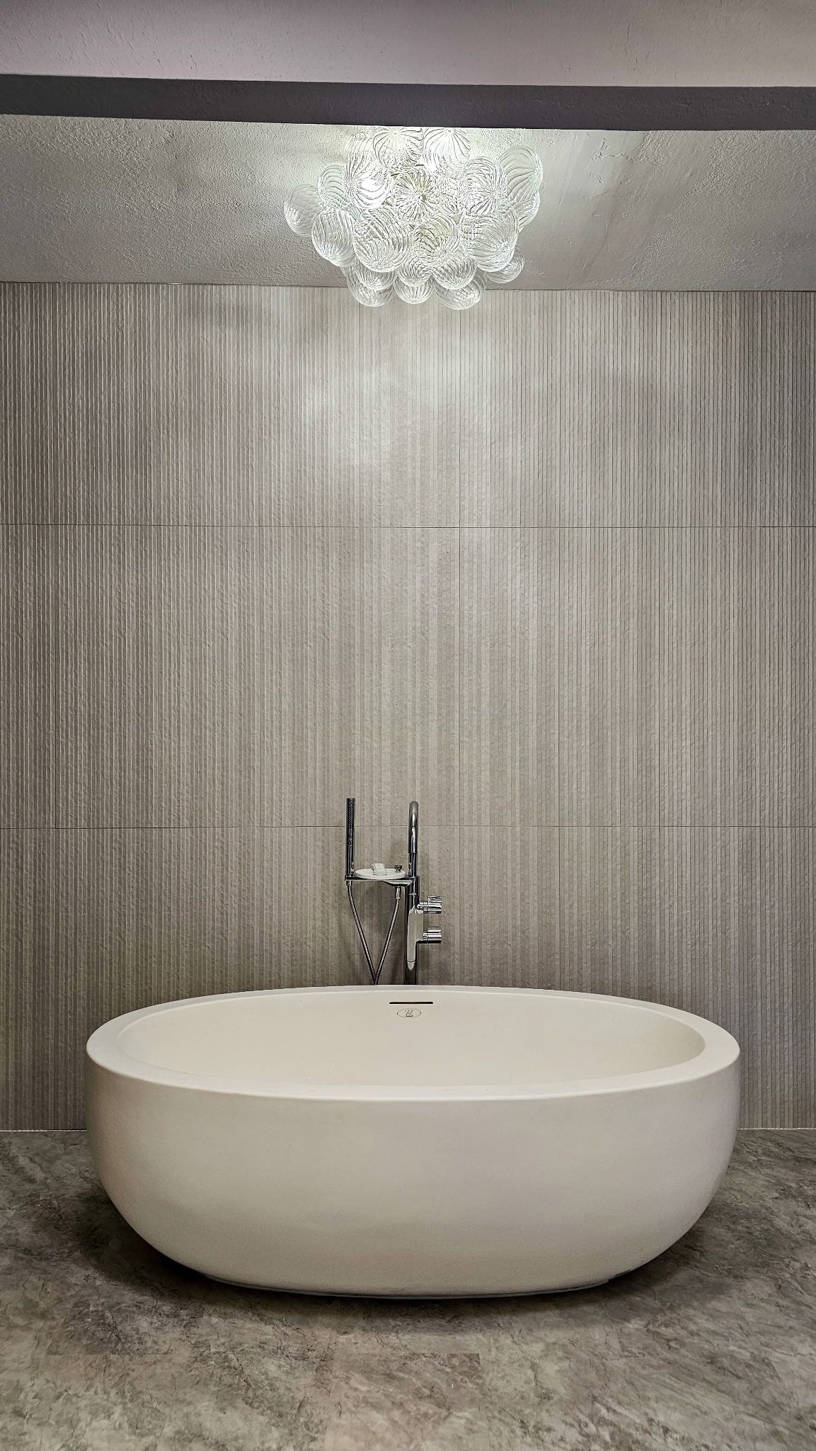 Modern bathroom with a freestanding oval bathtub and textured wall mosaic backdrop